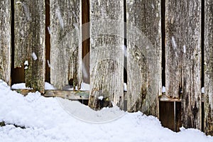 Winter background, falling snow and snow on ground in front of dilapidated wood fence