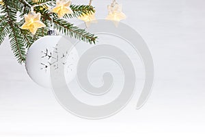 Winter background with green christmas tree branch, white decorative ball and glowing star lights