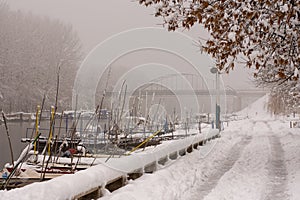Winter background with snow on the riverside with boats. Fogy winter day on the river with frost and snow