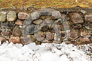 Russia, Lodeinoe Pole, December 2020. Snow and a fragment of a stone wall made of granite stones.