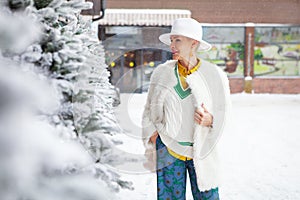 Winter bright fashion street style of middle age woman, wearing fedora hat, white faux fur coat clothes with colorful details