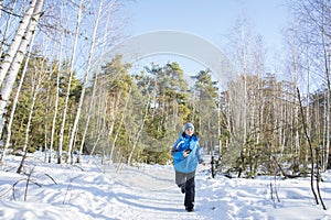 In winter, on a bright sunny day, a boy runs through the forest