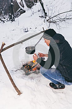 Winter camping, man warm up hands. Boiling water in pot. Wilderness and snow. Witnter time