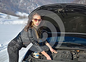 Winter car breakdown - young fashion woman trying to fix the car