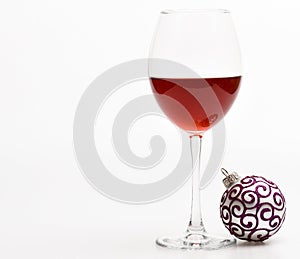 Winter celebration with alcohol drink. New year party concept. Wineglass with red liquid or wine and christmas ball