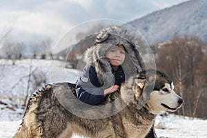 Winter childhood. Child embraced husky dog. Adorable little boy child with husky dog having fun on winter day.