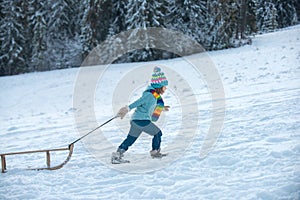 Winter children fun with sled. Winter outdoors games. Happy Christmas family vacation concept. Child sledging outside in