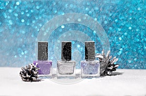 Winter Christmas background with two fir cones, glitter blue snowstorm and three nail polish bottles: purple, silver and blue