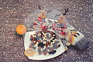 Winter Christmas composition. Coffee beans in chocolate on a plate, toy deer, wool socks and a candle on a wooden background and s