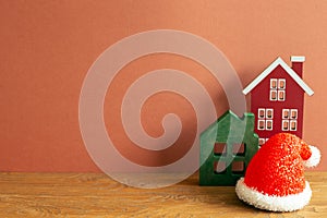 Winter christmas concept. Santa claus hat, house model on wooden table. red brown background