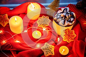 Winter Christmas holidays background with candles; christmas light; Cup of cocoa with marshmallow or hot chocolate near a window