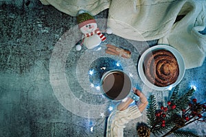 Winter Christmas holidays background with Cup of tea and wool scarf, cinnamon bun roll and snowman