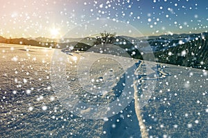 Winter Christmas landscape at dawn. Human footprint track path in crystal white deep snow through empty field, woody dark mountain