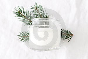 Winter, Christmas mockup-scene. Closeup of candle in glass jar with blank label. Blurred green fir tree branch, white