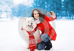 Winter, christmas, technology and people concept - woman and dog having fun takes selfie portrait on the smartphone