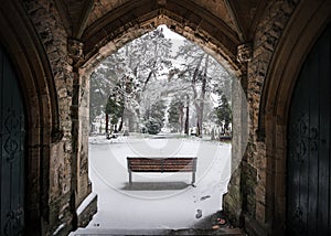Winter churchyard grave yard with solitary bench in falling snow winter scene archway beautiful and peaceful blanket snowfall Nott photo