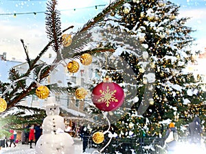 Winter city Christmas tree illuminated ,snowman and pine branch with gold confetti and red ball ,people walk ,snowy Tallinn old to