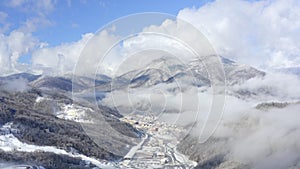 Winter city landscape between snowy mountains covered woodland. Aerial view snowy city in winter mountain valley. Drone view blue