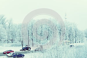 Winter city landscape. Trees covered with hoarfrost, a road with passing cars and a tractor for clearing roads.