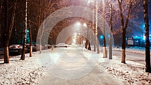 In the winter in city, a night street with phonories, a strong wind of snow. In the park, the road is covered with snow