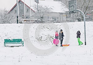 Winter cityscape, December, snowy streets, children, girls in bright clothes, sledding