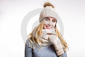 Winter close-up portrait of attractive young blonde woman wearing beige warm knitted hat with fur pompom and scarf snood. Girl