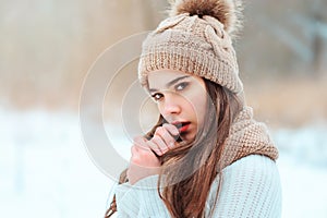 winter close up portrait of beautiful young woman in knitted hat and sweater walking in snowy park