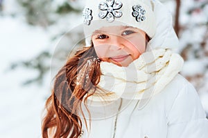 Winter close up portrait of cute dreamy child girl in white coat, hat and mittens playing outdoor in snowy winter forest