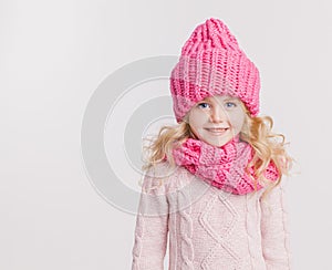 Winter clothes. Portrait of little curly girl in knitted pink winter hat and scarf