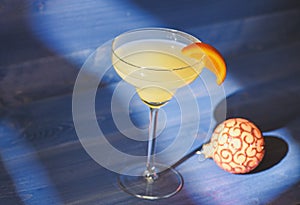 Winter cocktail drink concept. Alcohol cocktail margarita with piece of orange near christmas ball ornament on dark blue