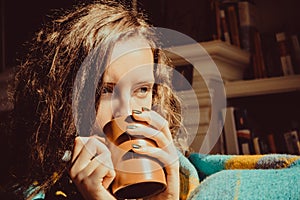 Winter cold sickness concept. Young freezing pensive woman with mug tea wrapped in warm plaid blanket. Natural light. Warm atmosph