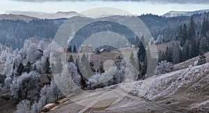 Winter coming. Picturesque foggy and moody morning scene in late autumn mountain countryside with hoarfrost on grasses, trees,