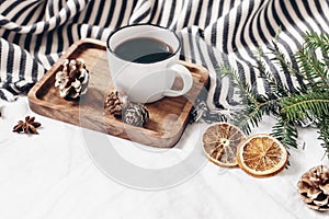 Winter composition. Breakfast in bed. Cup of coffee on wooden tray, wool blanket, fir tree branch, orange slices and