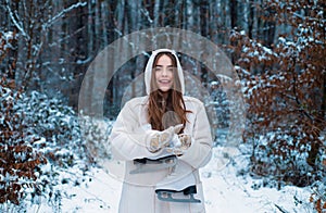 Winter concept. Beautiful girl in the winter forest in white down jacket. Joyful Beauty young woman Having Fun in Winter
