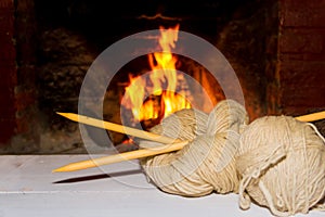 Winter concept knitting wool and tricot needles with fire from home on wood background