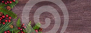 Winter corner border with evergreen branches, red berries and pine cones on a dark wood banner background