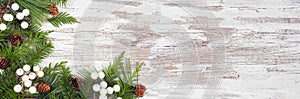 Winter corner border with evergreen branches, white berries and pine cones on a rustic white wood banner background photo