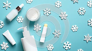 Winter cosmetic products set on blue background. Lipstick, cream jar, pump bottle, tube package mockup and snowflakes. Flat lay,