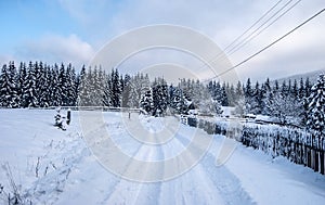 winter countryside with snow covered road, isolated house with fence, forest and blue sky with clouds