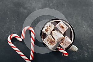 Winter cozy beverage. Glass with hot chocolate with marshmallow and candy cane on dark blue background. Top view with copy space