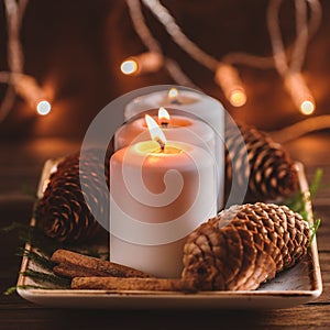 Winter cozy decoration with white burning candles on a wooden festive table and blurrred lights