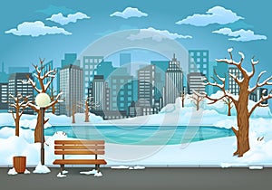 Winter day park. Snow covered wooden bench, trash bin and street lamp on an asphalt park trail with a frozen lake and cityscape.