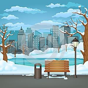 Winter day park. Snow covered wooden bench, trash bin and street lamp on an asphalt park trail with frozen lake and cityscape.