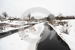 Winter daytime landscape with snow, river,trees and rustic house