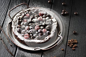 Winter dessert hygge style. Swedish chocolate cake kladdkaka with raw berries and icing sugar in vintage dish with vanilla pods