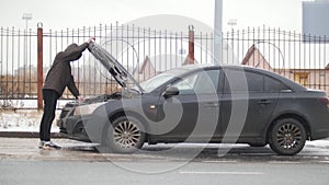 Winter driving. Car trouble. Car trouble on a snowy country road. A young man closes down the hood and gets in the car