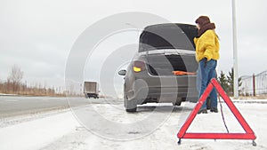 Winter driving. Car trouble. An emergency sign. Car trouble on a snowy country road. A young woman call the rescue