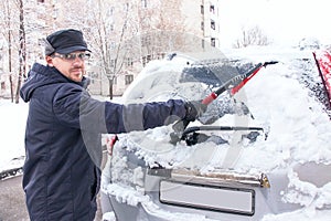 Winter driving. The man is cleaning car's window from snow.