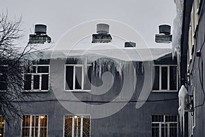 Winter on the edges of the roofs hang freezing icicles of large sizes. Melting and freezing snow on the roofs of houses. White