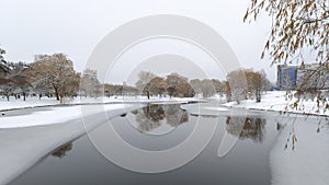 In winter everything is covered with snow, and the water channel in the city park is partially covered with ice. Willows and birch